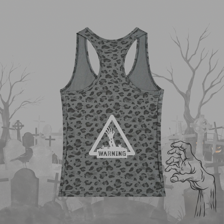 A gray racerback tank top with a dark gray leopard print pattern and a white warning sign graphic on the front, displayed against a spooky graveyard background with a zombie hand illustration.