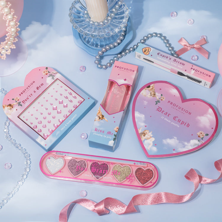 Gemstones in different sizes, eyeshadows palette in 5 shades (gold, silver, white, red) in the shape of a love heart and pearls in the background, ribbons, and love heart shaped pad