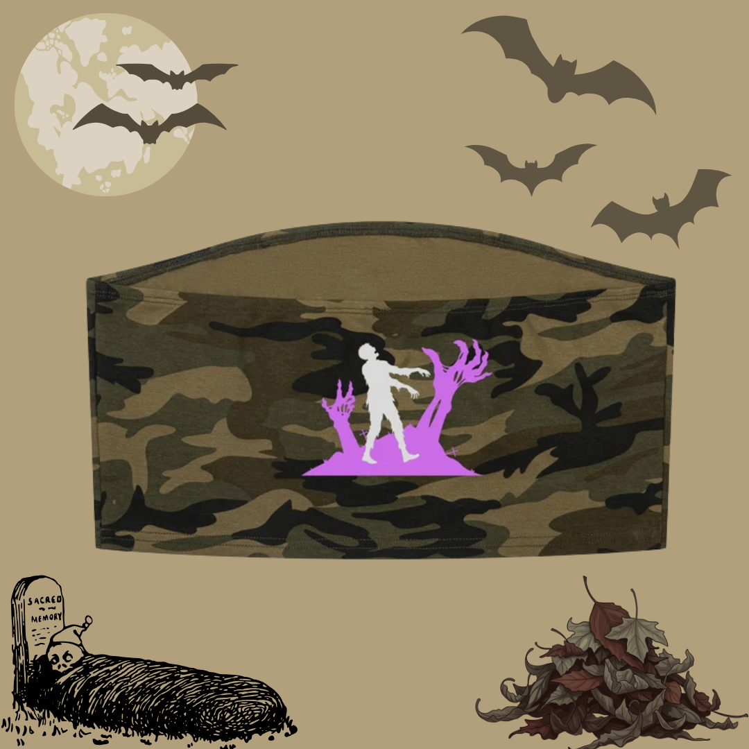 A Halloween-themed decorative cropped top with a camouflage pattern and a central graphic of a white figure walking toward purple zombie hands and branches. The cropped top is displayed on a beige background decorated with bats, a full moon, a tombstone, and autumn leaves.