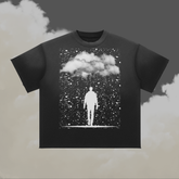 A black short-sleeve crewneck t-shirt featuring a white graphic print of a figure standing under a cloud amidst falling rain, displayed against a cloudy grey and beige background