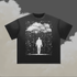 A black short-sleeve crewneck t-shirt featuring a white graphic print of a figure standing under a cloud amidst falling rain, displayed against a cloudy grey and beige background
