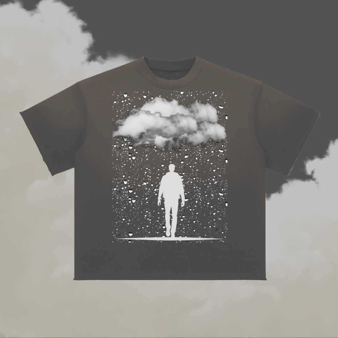 A dark charcoal gray t-shirt featuring a white graphic print of a silhouette of a man standing under a cloud with falling snow, displayed against a cloudy grey background.