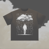 A dark charcoal gray t-shirt featuring a white graphic print of a silhouette of a man standing under a cloud with falling snow, displayed against a cloudy grey background.