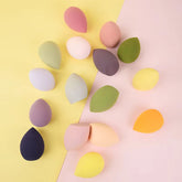 A group of makeup sponges and beauty blenders that are multicoloured on a yellow and baby pink background.