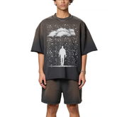A man wearing a dark grey sun fade raw edge t-shirt, with raindrops on it and clouds and a silhouette of man walking. 