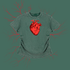 A short-sleeve t-shirt in a washed, heathered sage green color, featuring a prominent red anatomical heart graphic on the chest. The shirt is displayed against a solid sage green background with faint red branching line art extending outward.