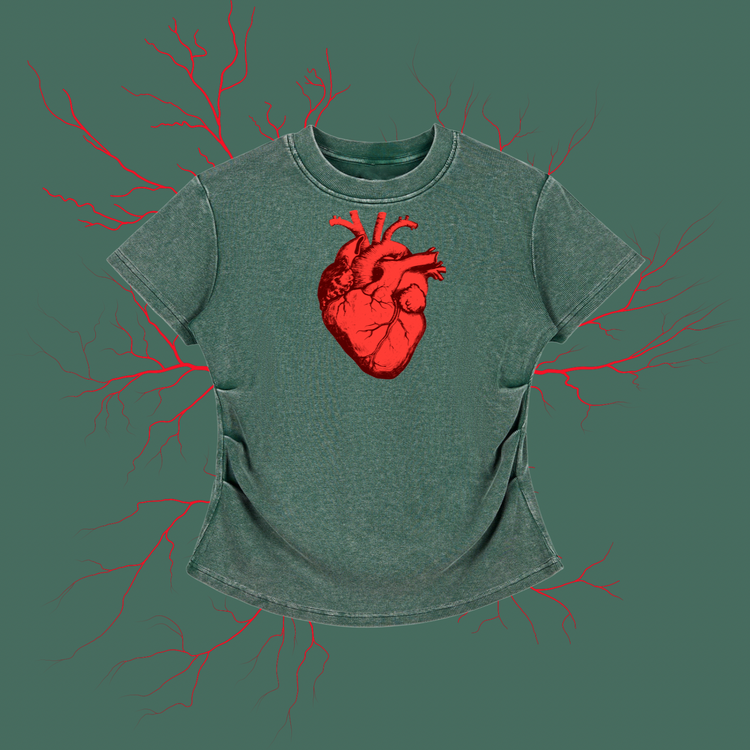 A short-sleeve t-shirt in a washed, heathered sage green color, featuring a prominent red anatomical heart graphic on the chest. The shirt is displayed against a solid sage green background with faint red branching line art extending outward.