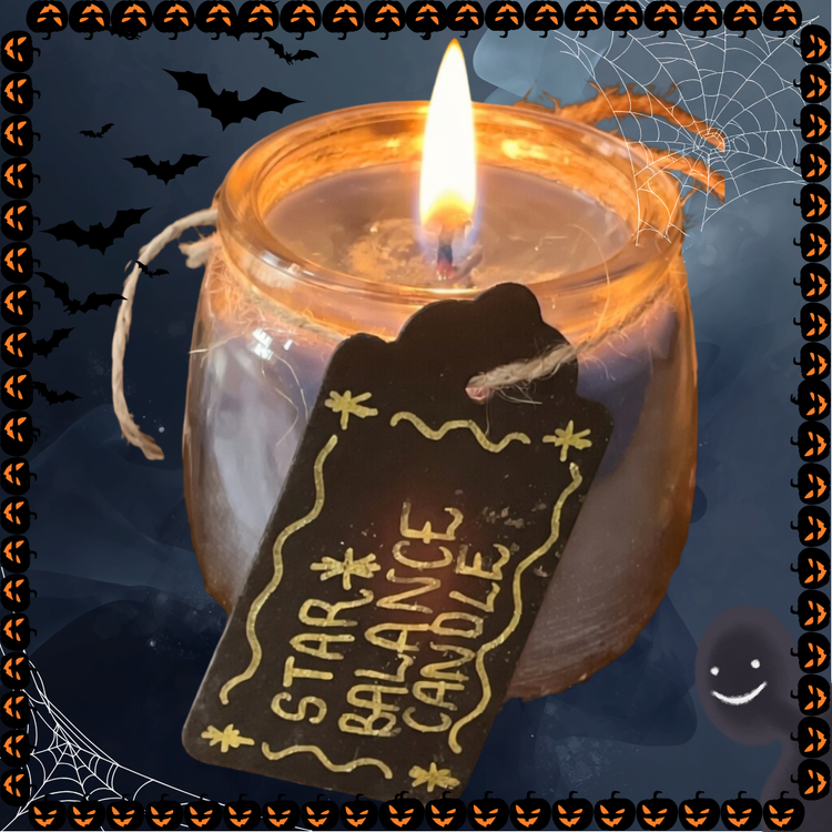 Black dark grey candle in a glass jar with a cotton wick that is lit, with a tweed string with a black paper tag with the text "Star balance candle" on a dark grey background with bats and cobbed webs and Halloween pumpkins.