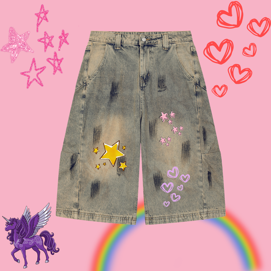 Blue jean shorts that have clean cut hem and reverse vintage wash with two pockets and belt hooks. There are yellow stars on it and pink star, and pink love hearts. The shorts go above the knee and are loose fit. The background is light pink with red love hearts, pink stars and purple unicorns and rainbow.