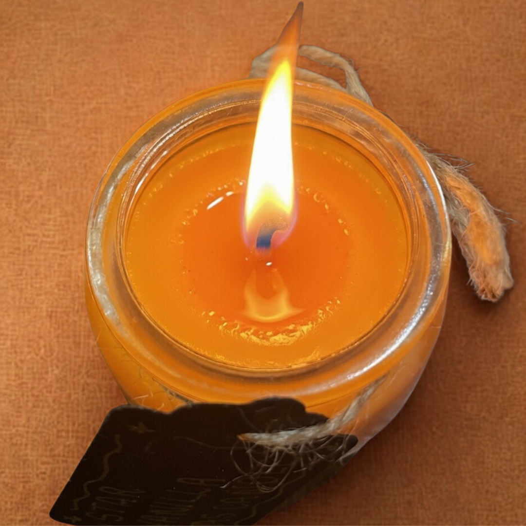 Candle in a glass jar with a cotton wick lit with a tweed string with a black paper tag an orange background 