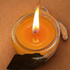 Candle in a glass jar with a cotton wick lit with a tweed string with a black paper tag an orange background 