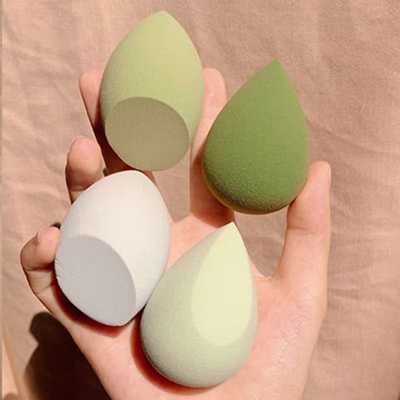 Four green makeup sponges held in a hand against a beige background