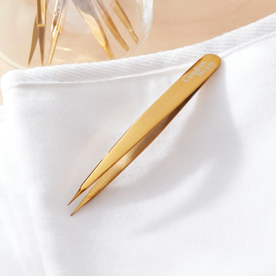 Gold-coloured tweezers on a white fabric background