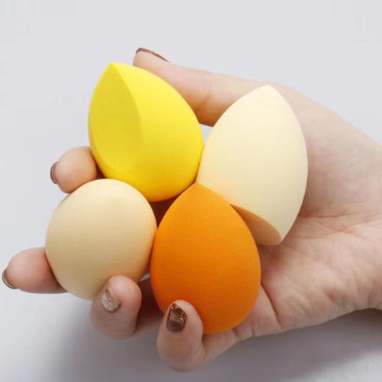 Hand holding four colourful makeup sponges on a white background