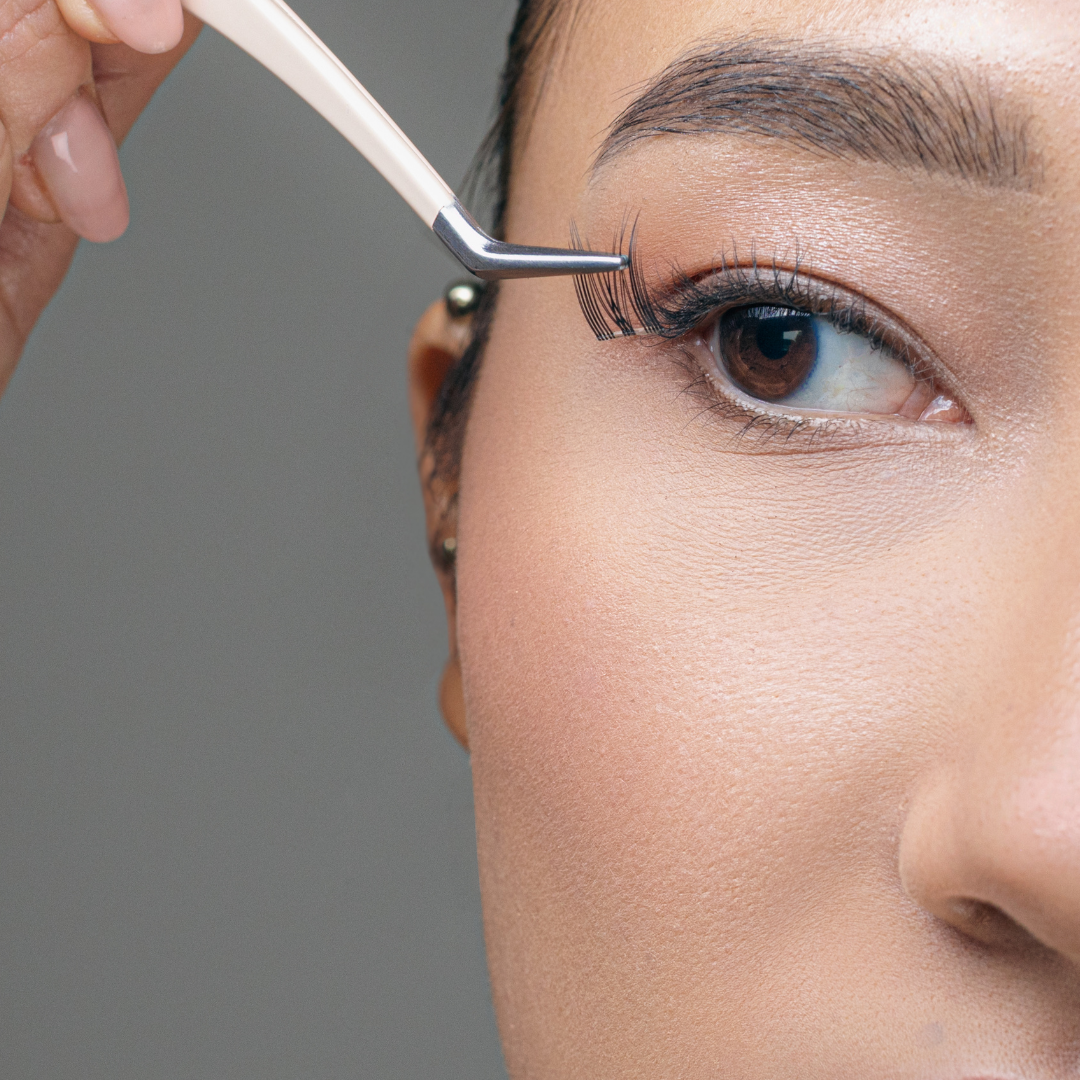 Person grooming their eyebrow with a small brush against a neutral background