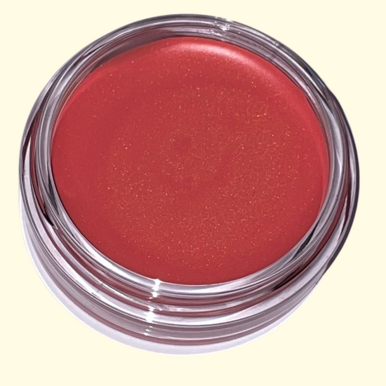 Red cosmetic cream blush in a clear container on a light yellow background