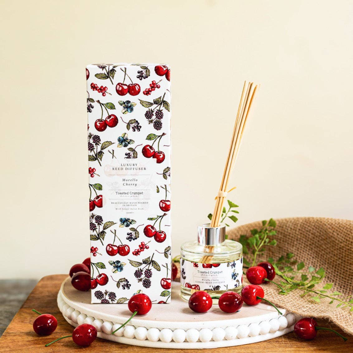 Reed diffuser with packaging featuring cherry design on a wooden surface.