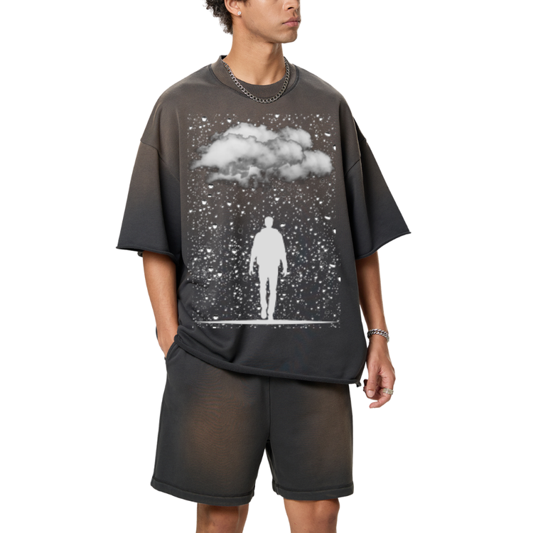 A man wearing a dark grey sun fade raw edge t-shirt, with raindrops on it and clouds and a silhouette of man walking. 
