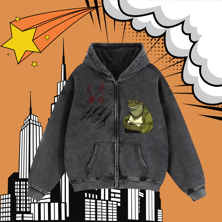 A dark gray zip-up hoodie with a frog graphic and red claw marks, displayed against a comic-book style background with an orange sky, white clouds, and black-and-white city buildings.